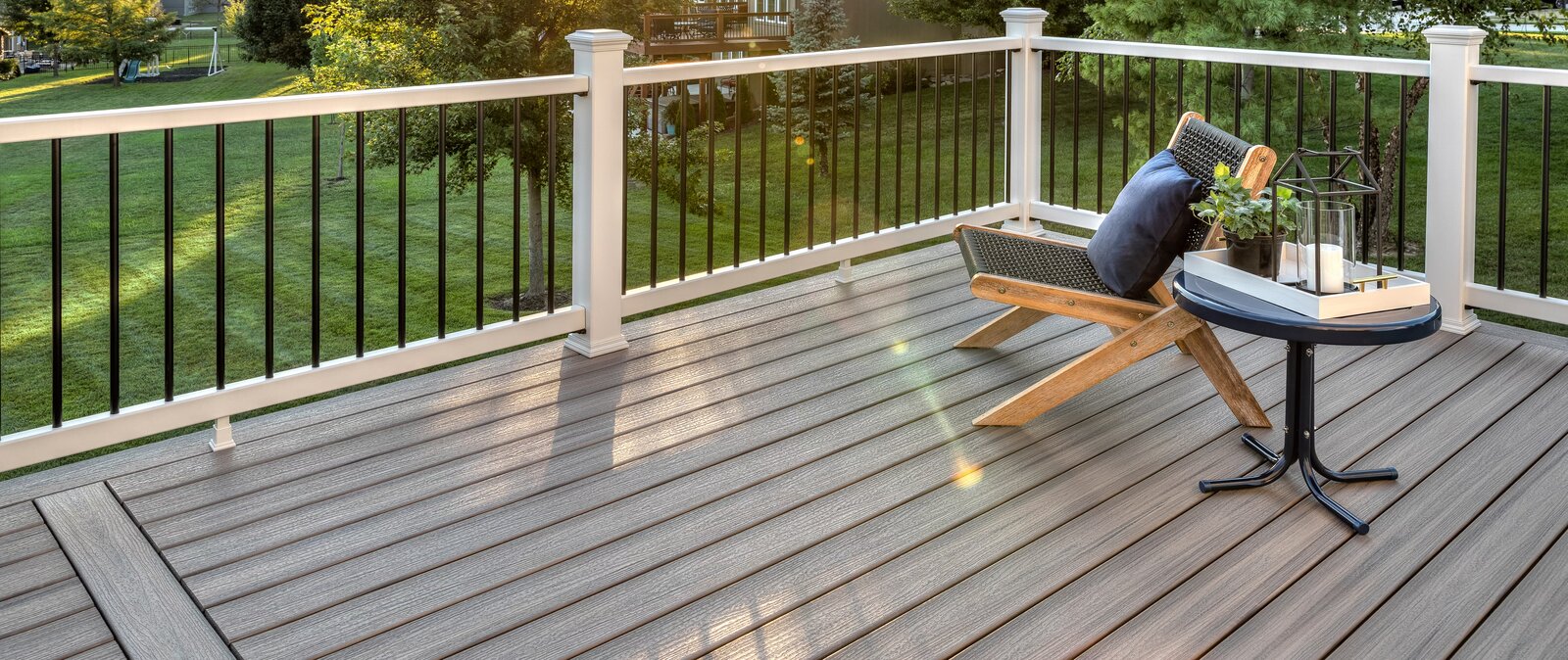 Backyard Trex composite deck with grey board pattern, white posts, and black aluminum baluster railing overlooking a lawn