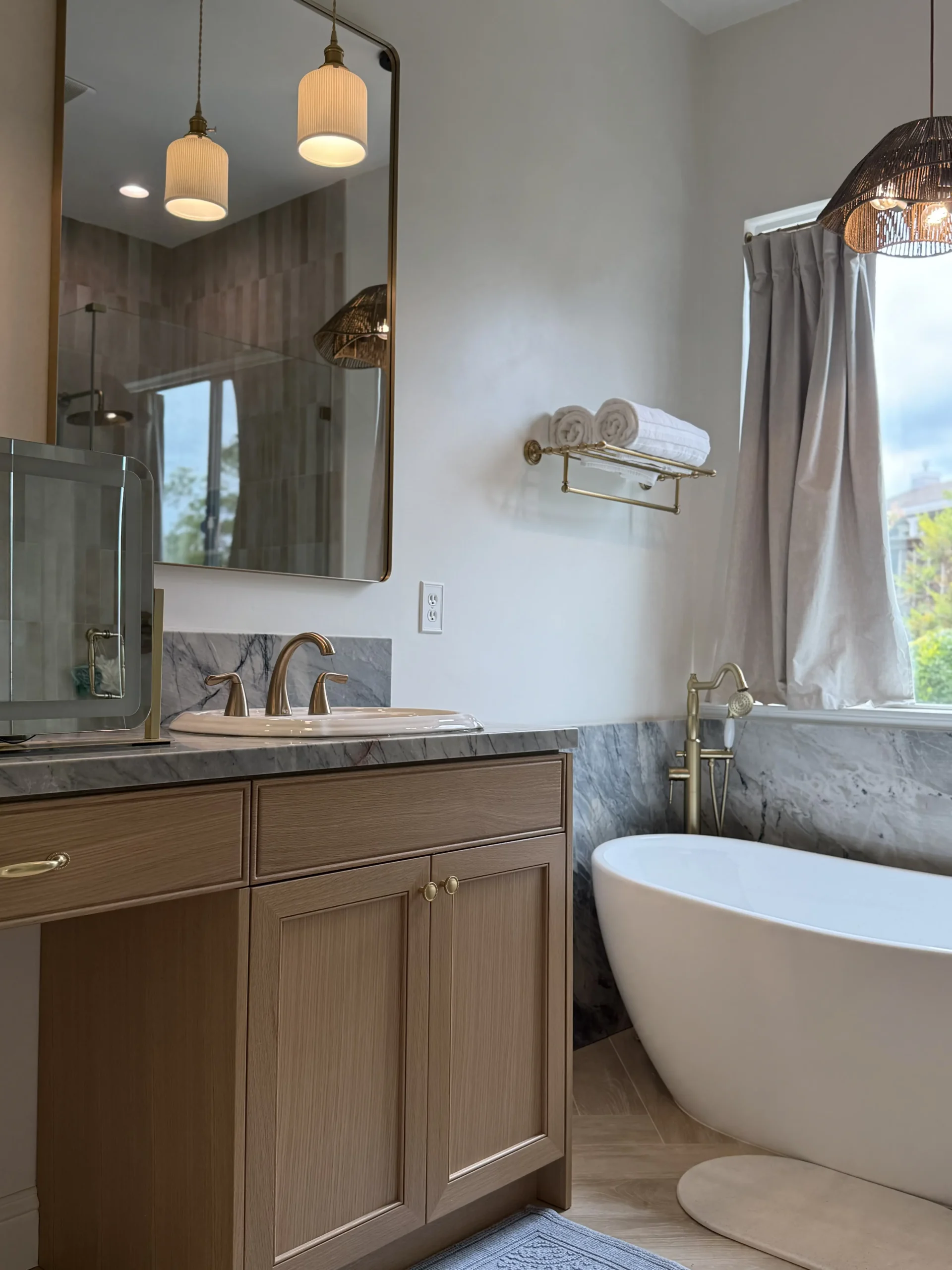 Spa bathroom with arched mirror, marble vanity backsplash, freestanding soaking tub, and woven pendant lights