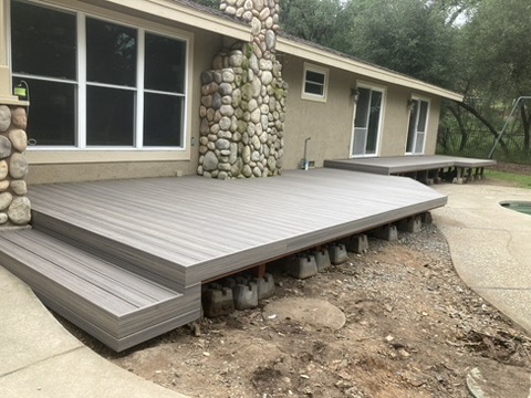 Low-profile composite deck addition with river-rock stone column accent against a hillside home