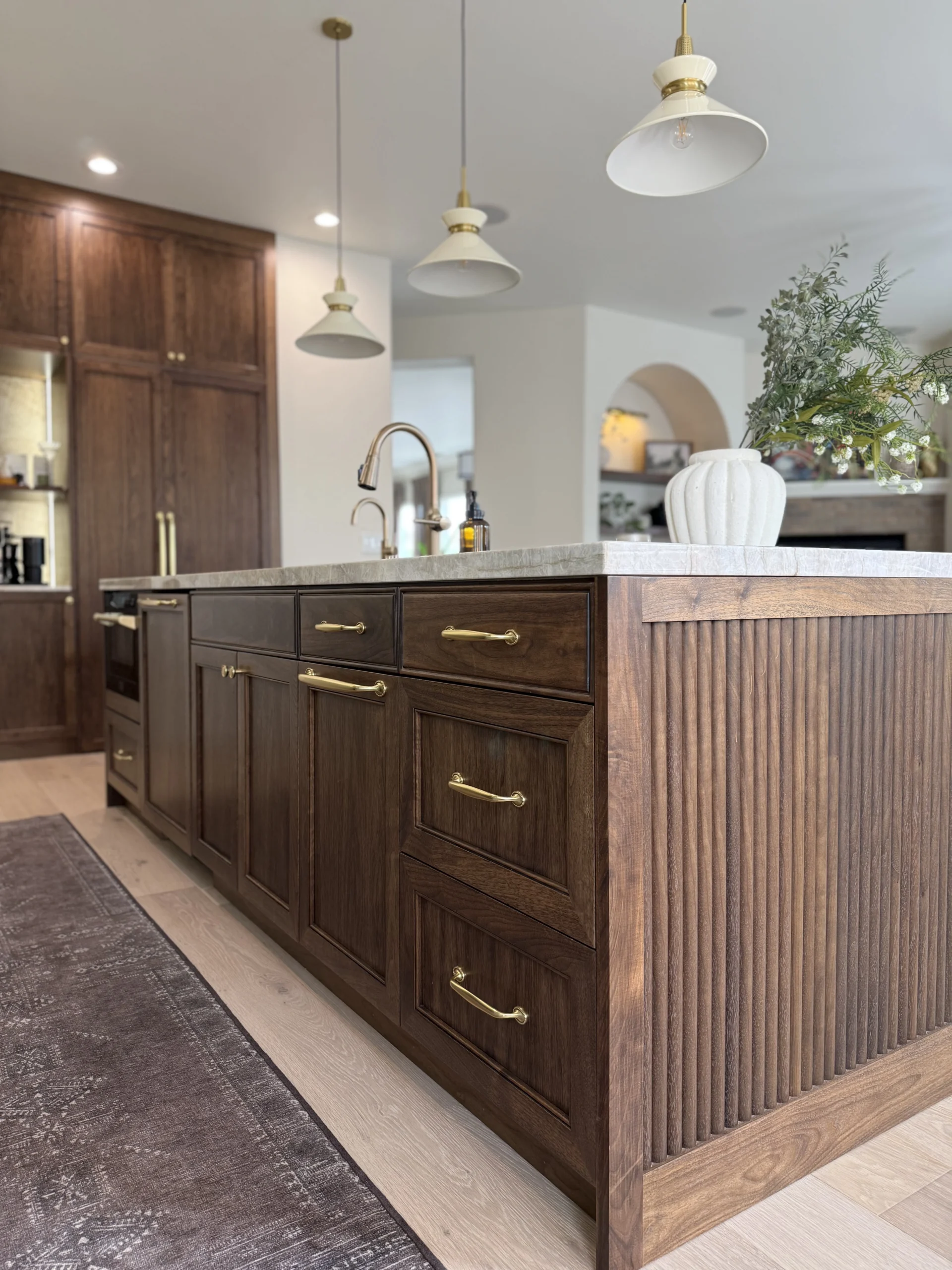 Custom walnut kitchen island with fluted side panels, brass hardware, and white pendant lighting