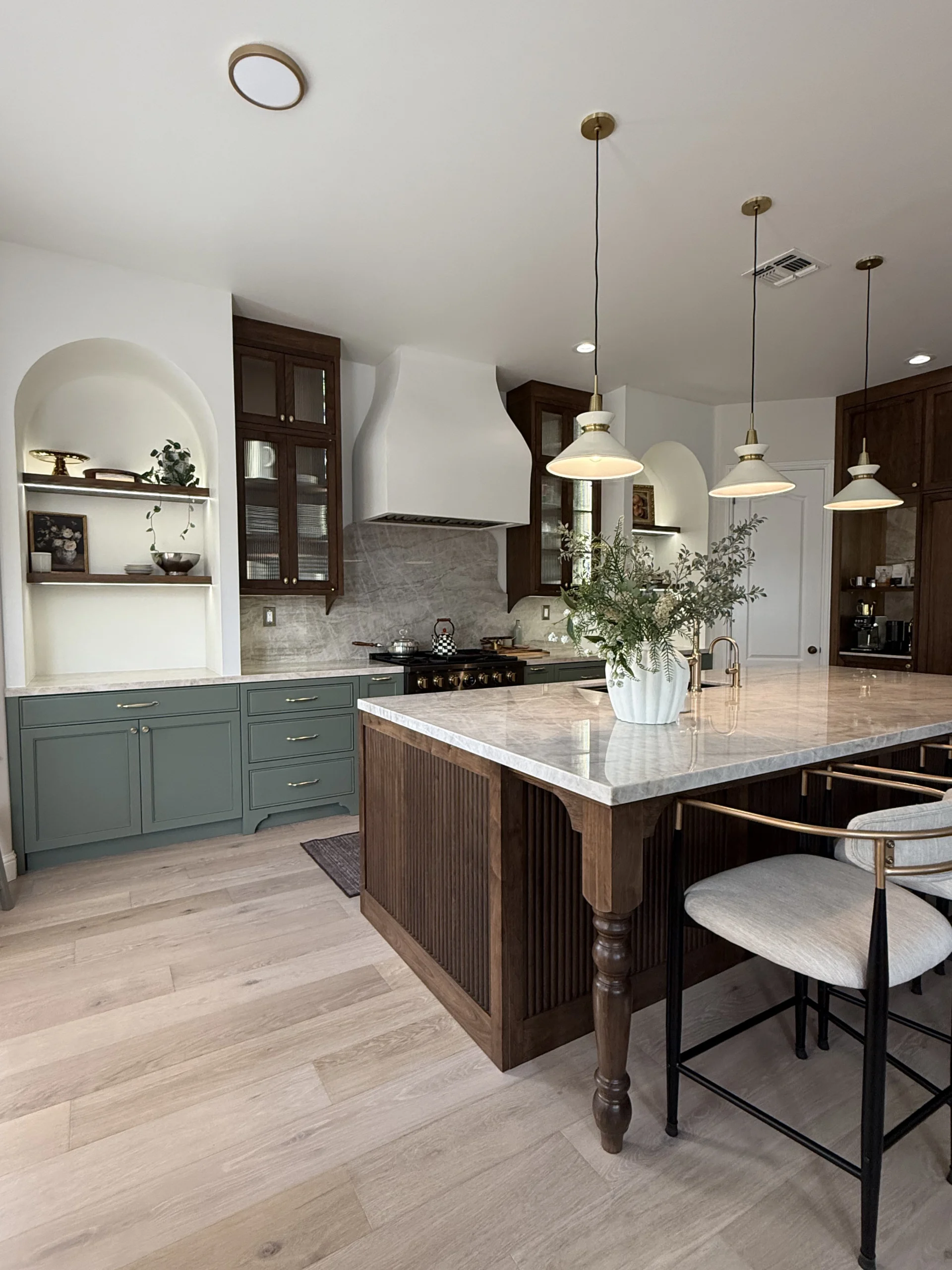 Finished custom kitchen with sage green shaker cabinets, walnut accents, marble waterfall island, and brass pendant lighting